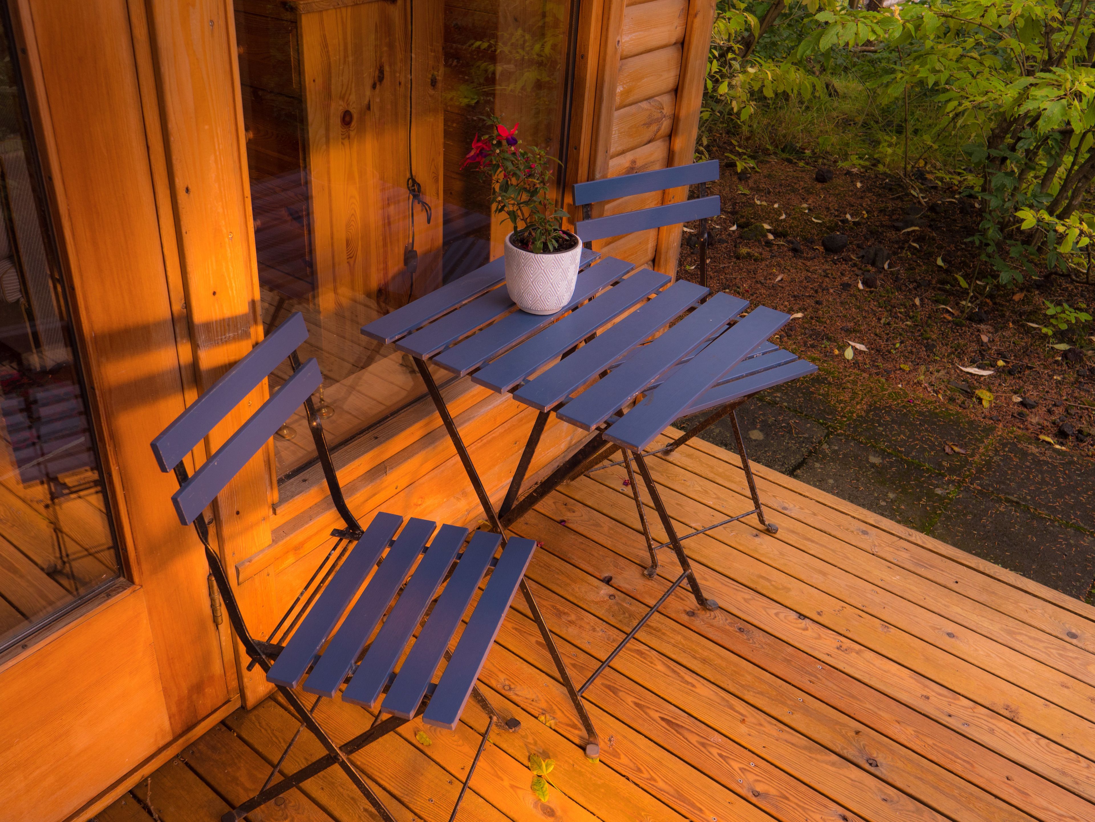 A wooden deck with a metal table and two blue chairs.