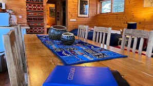 Interno di una baita in legno con un tavolo da pranzo apparecchiato per quattro persone, con tovaglia blu e una scatola blu etichettata 'GESTABOK'.
