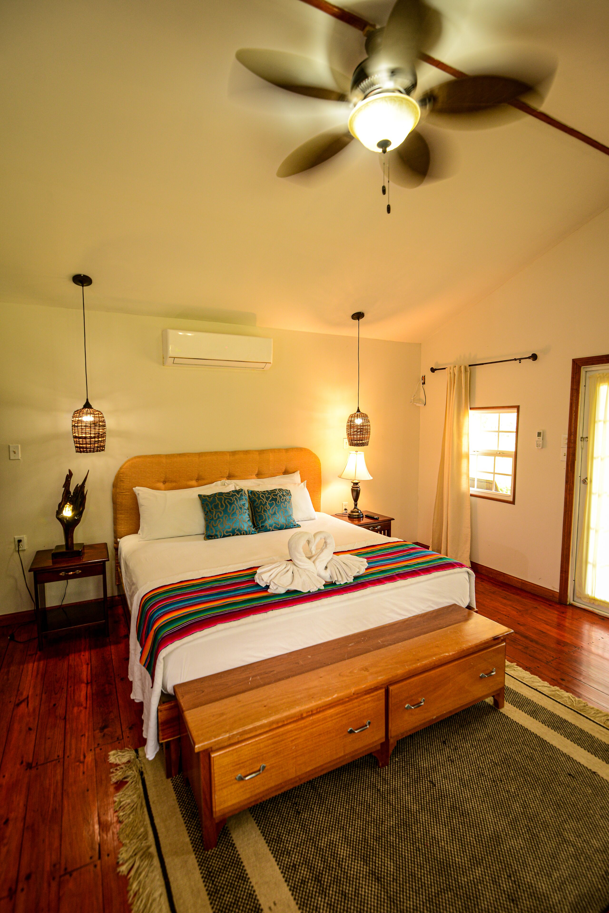 A bedroom with a wooden bed, a ceiling fan, a bedside lamp, and a window with curtains.