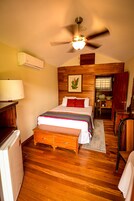 Un dormitorio con cama, suelo de madera, ventilador de techo y un escritorio pequeño con lámpara.