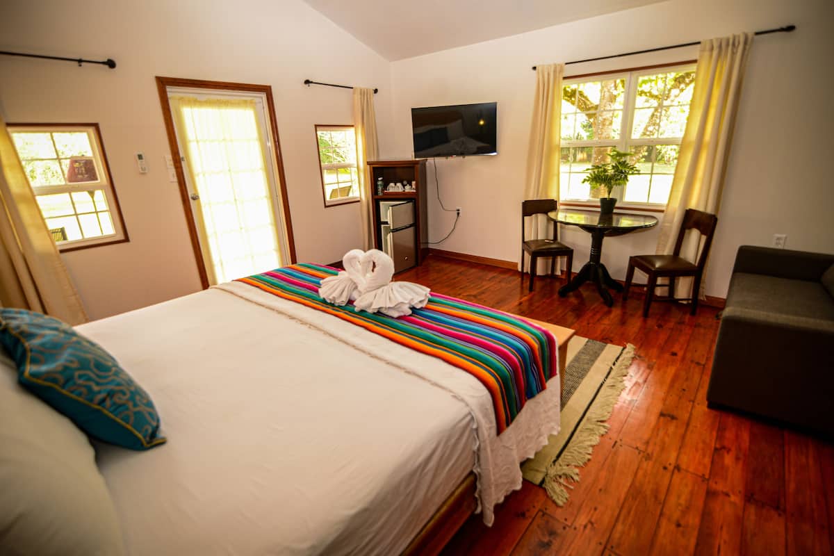 A hotel room with a bed, a TV mounted on the wall, a small table with chairs, and a window with curtains.