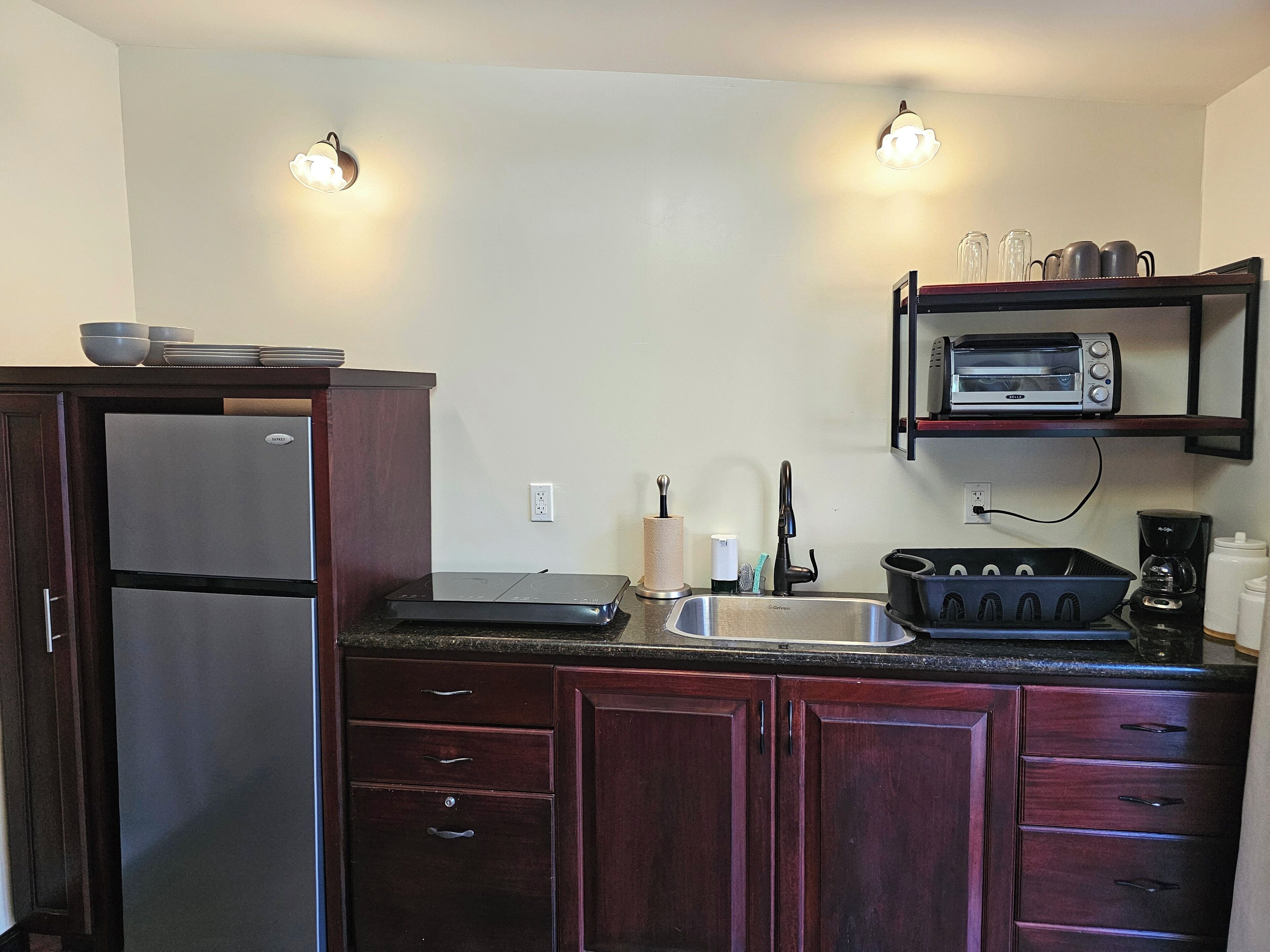 A kitchen with a refrigerator, a toaster oven, a sink, and a coffee maker.