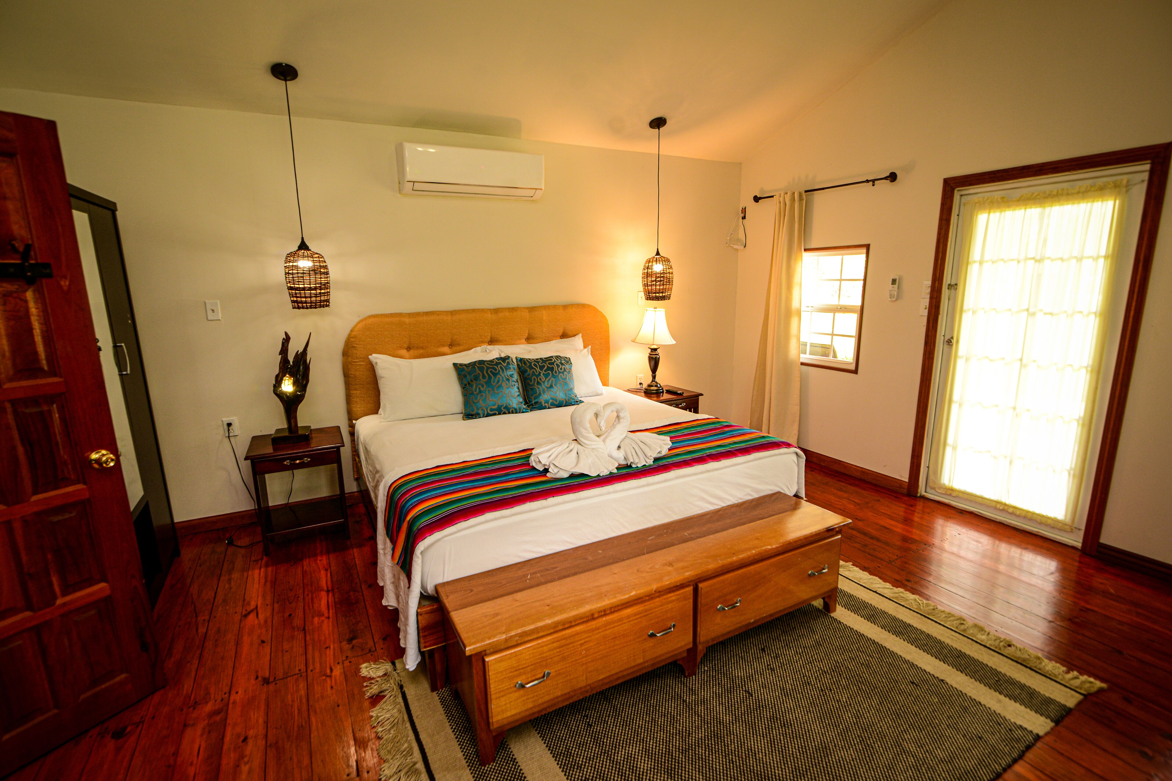 A bedroom with a wooden bed, a bench, a bedside table, a lamp, and a window with curtains.