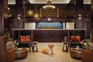 A lobby with a reception desk, two armchairs, a coffee table, and a dog sitting on the floor. - Hotel Northland, Autograph Collection (Green Bay)