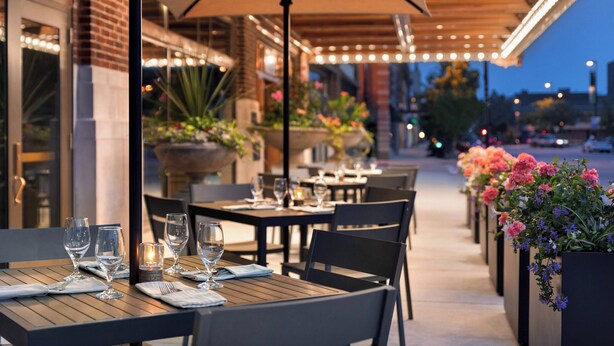 An outdoor dining area with tables and chairs, umbrellas, and potted plants. - Hotel Northland, Autograph Collection (Green Bay)