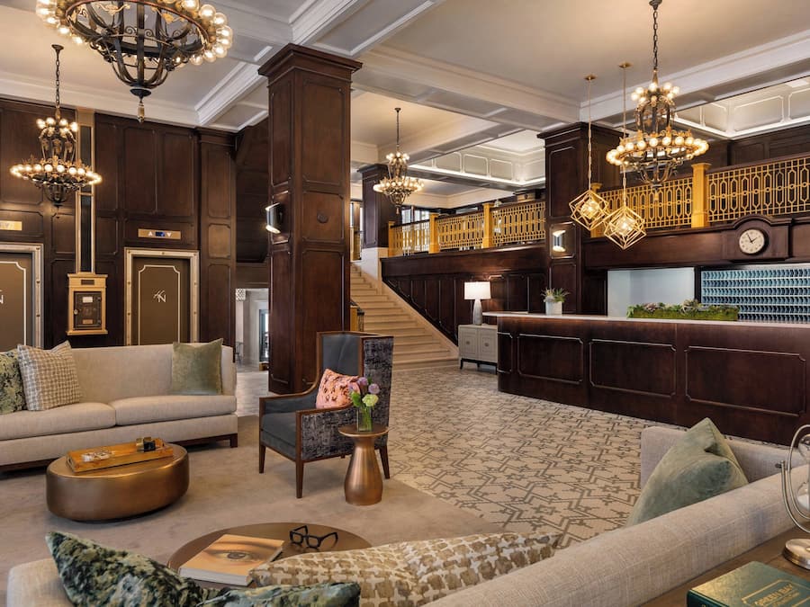 A spacious lobby with a grand staircase, a reception desk, and elegant chandeliers.