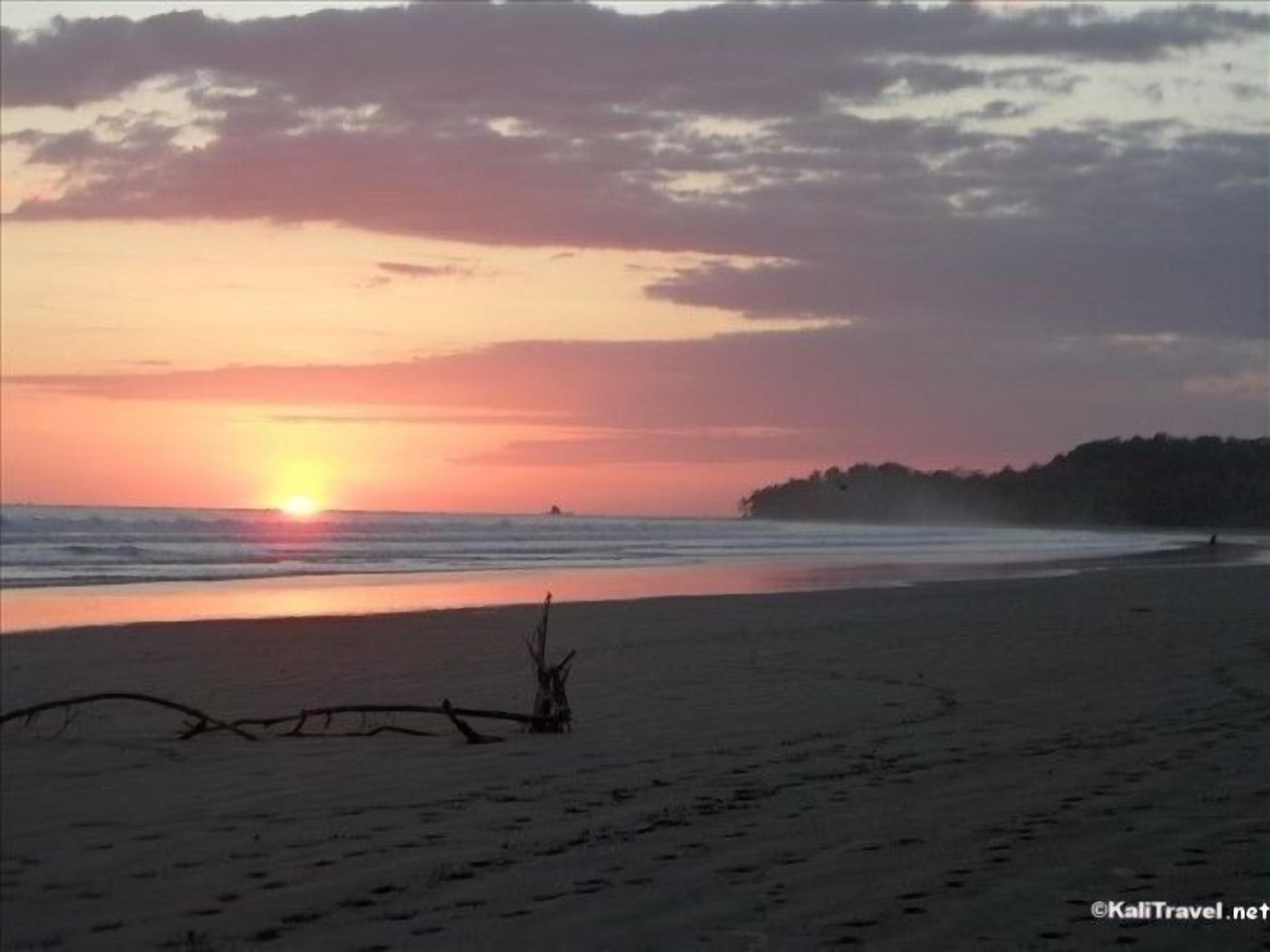 A beach at sunset with calm waters and a clear sky.