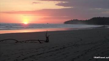 A beach at sunset with calm waters and a clear sky.