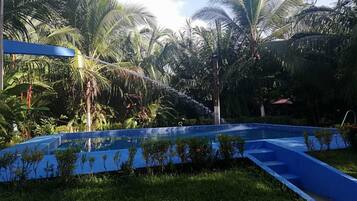 A swimming pool with blue steps and a water feature, surrounded by lush greenery and palm trees.