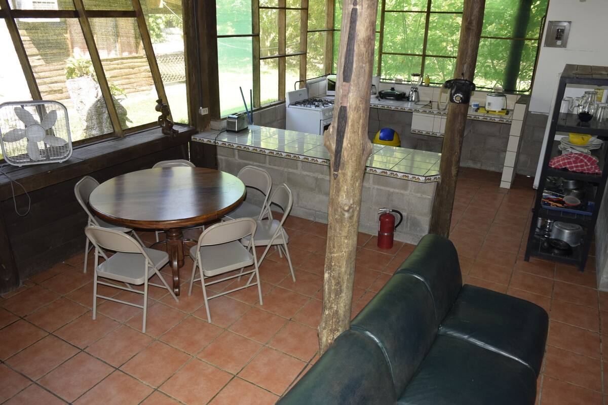 A dining area with a round table and chairs, a green couch, and a kitchen area with a stove and sink.