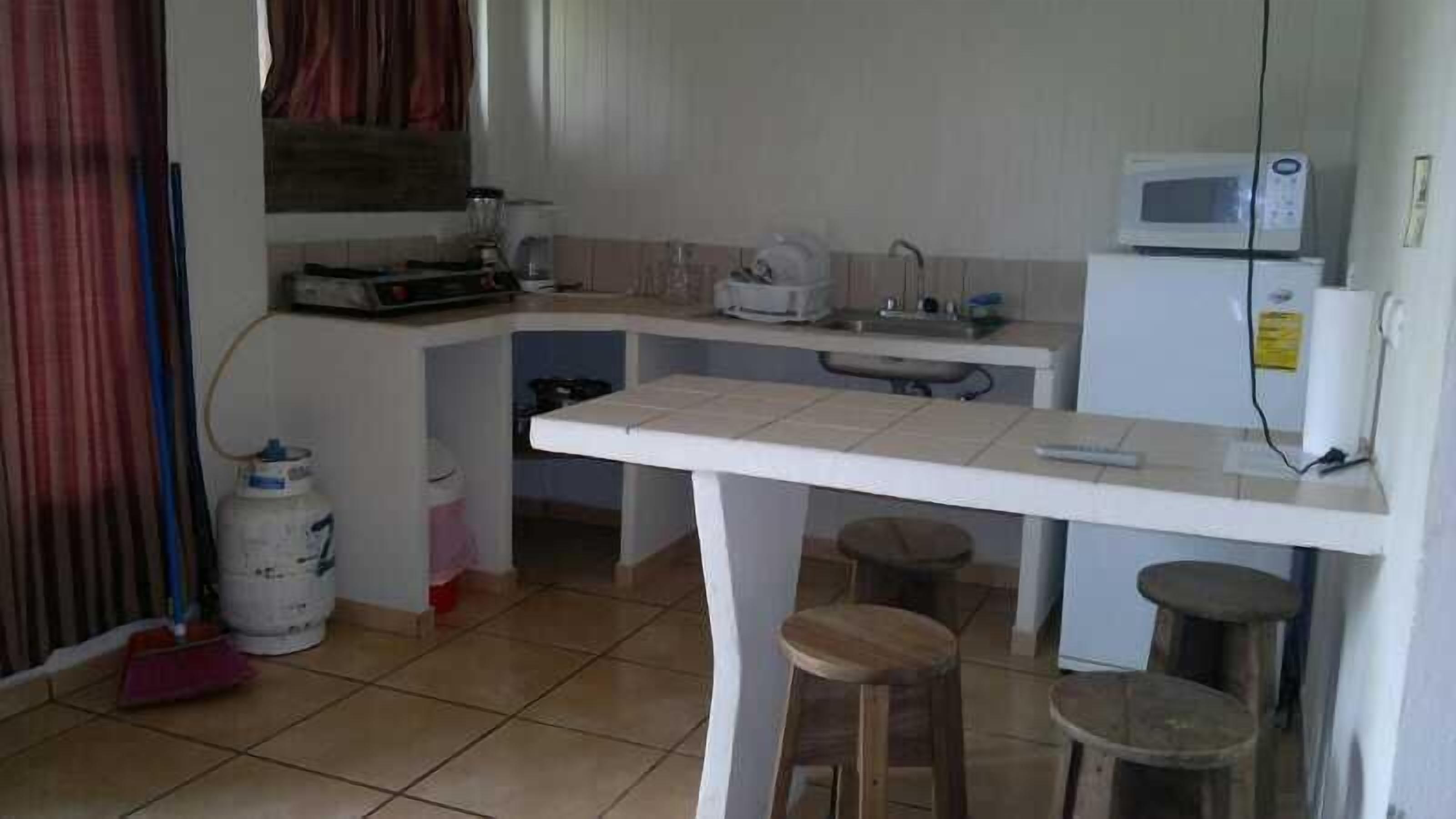 A compact kitchen with a white countertop, a microwave, a sink, and stools.