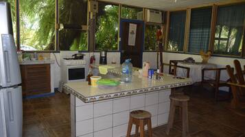 Una cocina con una isla central, taburetes de madera, un refrigerador, una estufa y un ventanal con vistas al verdor.