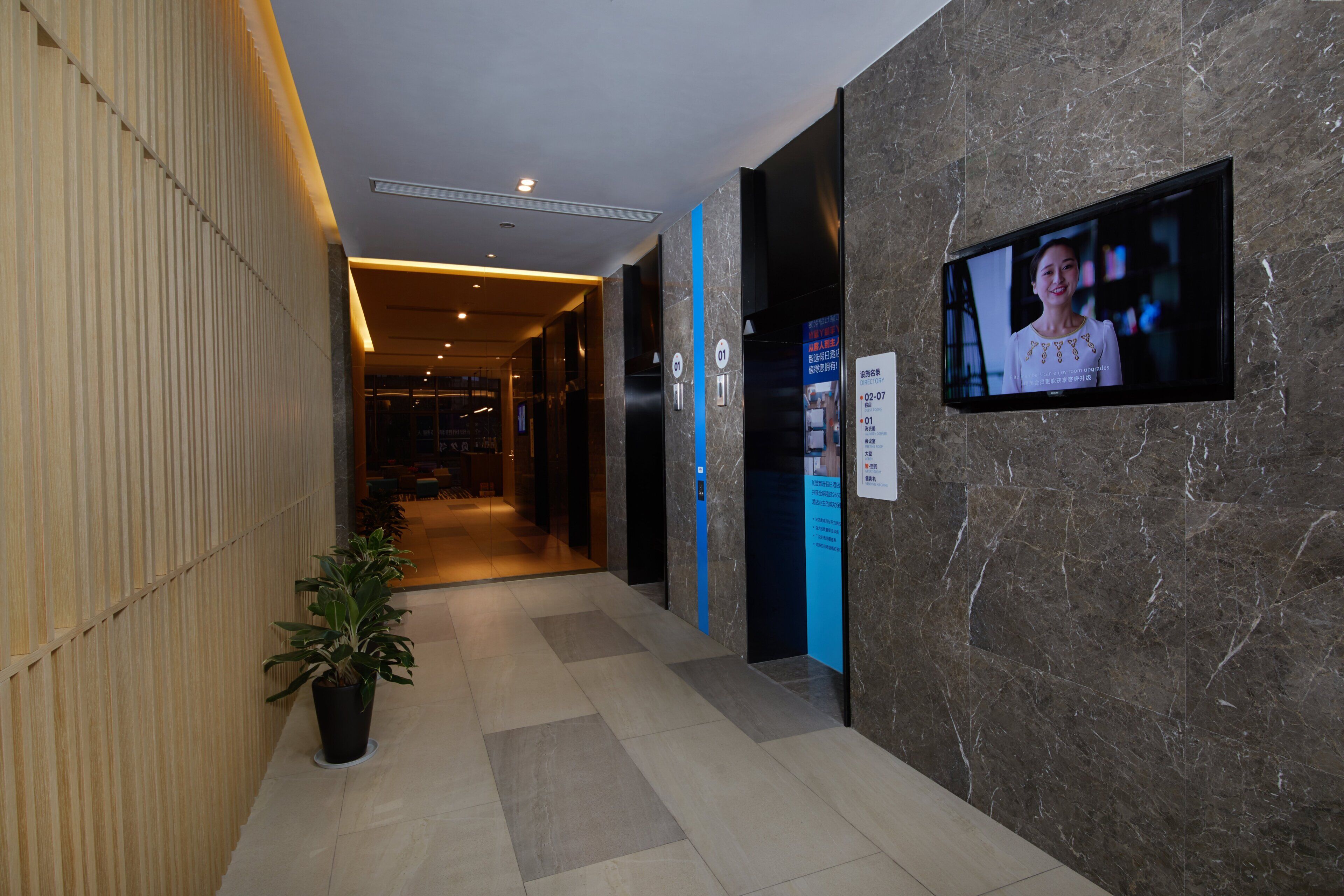 Un hall de hotel con mostrador de recepción, una pantalla de televisión y un cartel con indicaciones.