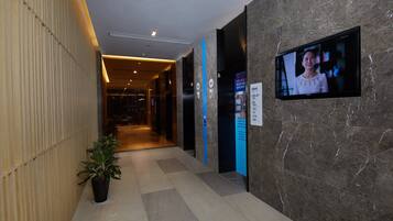 Un hall de hotel con mostrador de recepción, una pantalla de televisión y un cartel con indicaciones.
