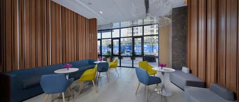 Un interior moderno con una zona de estar que incluye un sofá azul y sillas amarillas, una mesa blanca y una lámpara decorativa en el techo.