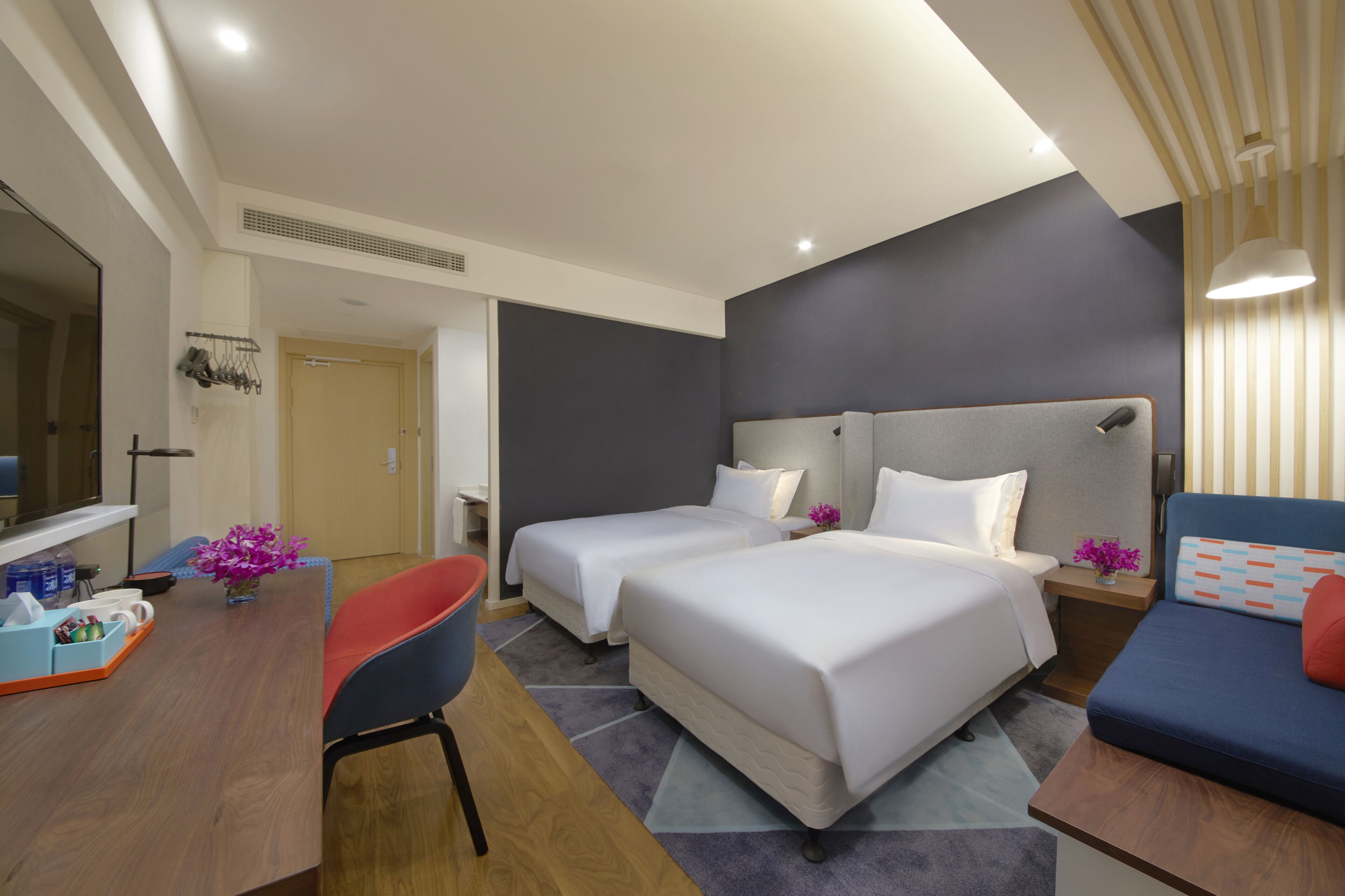 A hotel room with two beds, a desk, a chair, and a sofa.