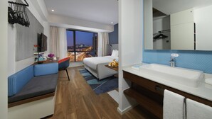A modern hotel room with a large bed, a seating area, a bathroom with a sink, and a city view. - Holiday Inn Express Zhangjiagang East by IHG (Suzhou)