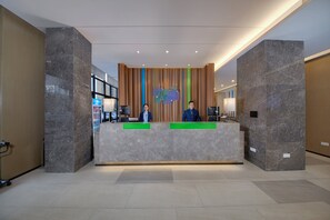 A reception desk with two staff members, a vertical wooden panel wall, and a marble floor. - Holiday Inn Express Zhangjiagang East by IHG (Suzhou)