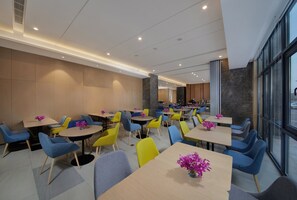 A modern dining area with multiple tables and chairs, a kitchen in the background, and large windows. - Holiday Inn Express Zhangjiagang East by IHG (Suzhou)