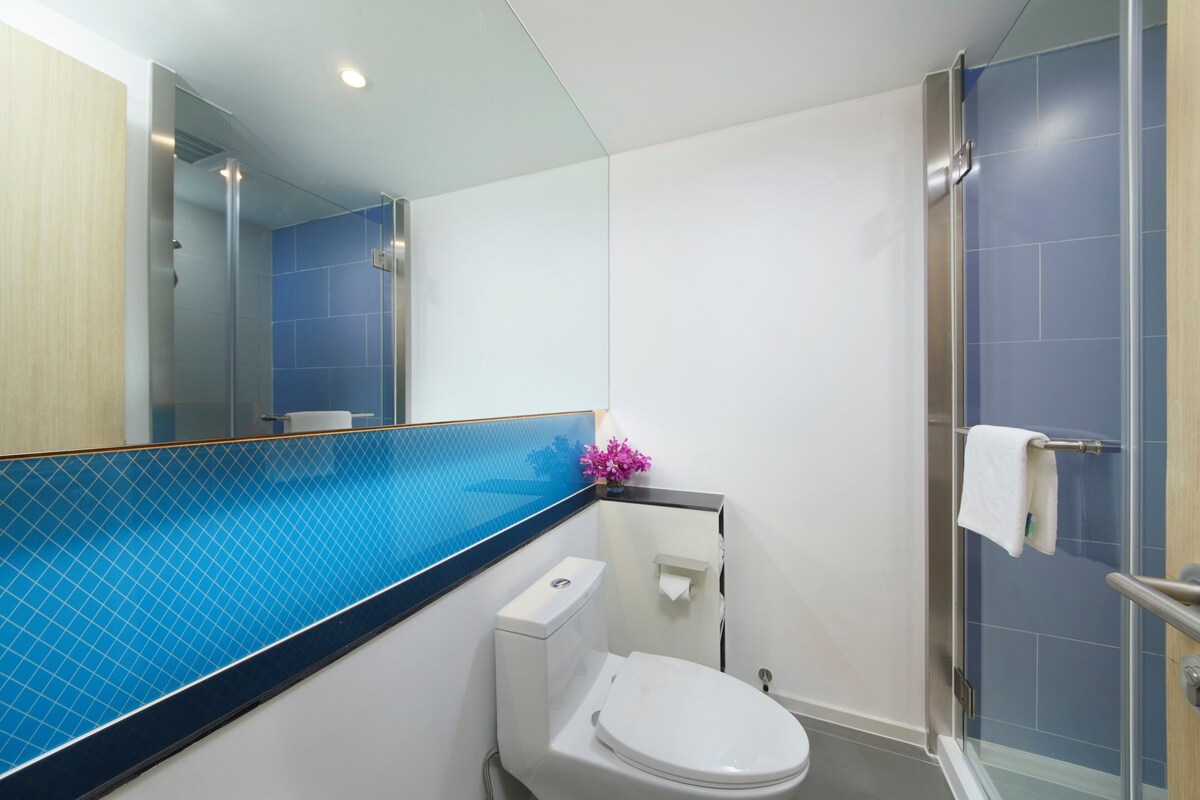 A modern bathroom with a blue-tiled shower enclosure, a white toilet, and a mirror above the sink.