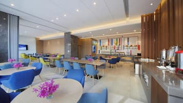 Un restaurante moderno con varias zonas de estar, incluyendo mesas redondas y cabinas, además de un área de bar con una máquina de café.