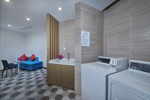 A compact hotel room with a kitchenette, a washing machine, a sofa with cushions, and a patterned floor. - Holiday Inn Express Zhangjiagang East by IHG (Suzhou)