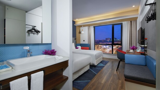 A modern hotel room with a large window, a bathroom with a sink and mirror, a bed, and a seating area with a view of the city. - Holiday Inn Express Zhangjiagang East by IHG (Suzhou)