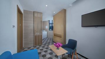 Habitación de hotel con piso a cuadros, un sofá azul, una mesita con un florero, un televisor montado en la pared y un panel de madera.