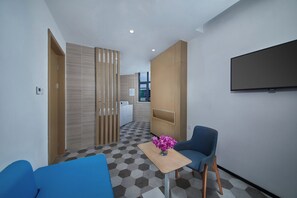 A hotel room with a checkered floor, a blue sofa, a small table with a vase, a television mounted on the wall, and a wooden partition. - Holiday Inn Express Zhangjiagang East by IHG (Suzhou)