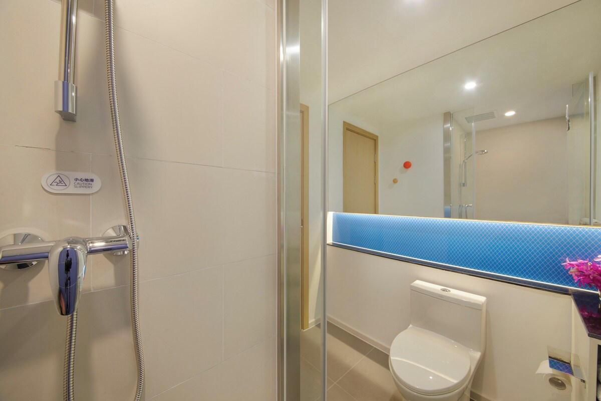 A bathroom with a glass shower enclosure, a toilet, and a mirror with a blue-tiled countertop.
