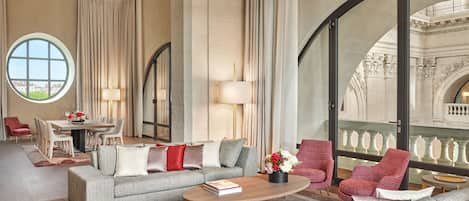 A spacious living room with a large window, a dining area, and a balcony with ornate railings.