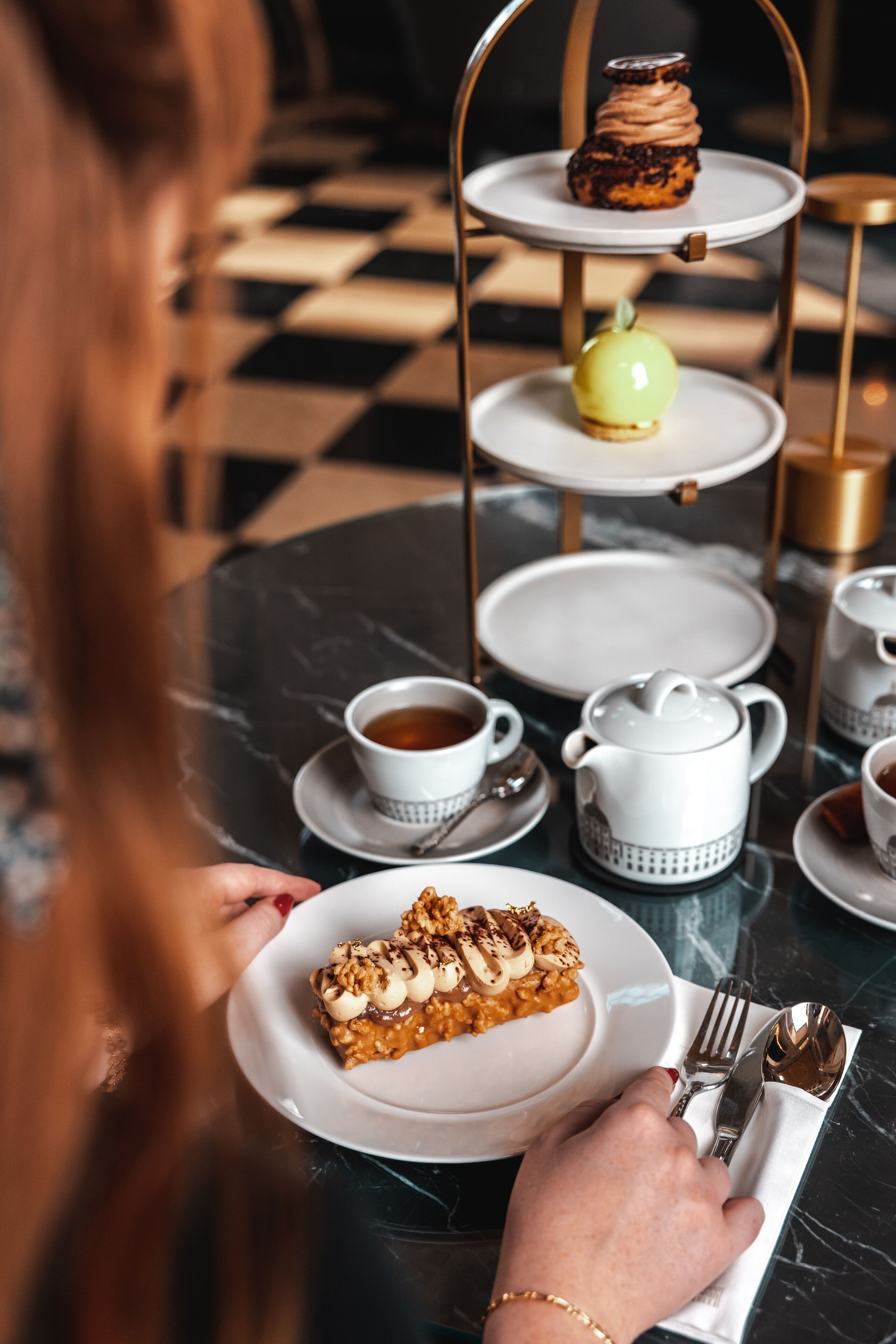 A table with a dessert plate, a teapot, cups, and a tiered dessert stand.