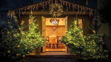 Una cabaña de madera con dos árboles de Navidad en primer plano, una cabeza de ciervo en la pared y una mesa con sillas en el interior.