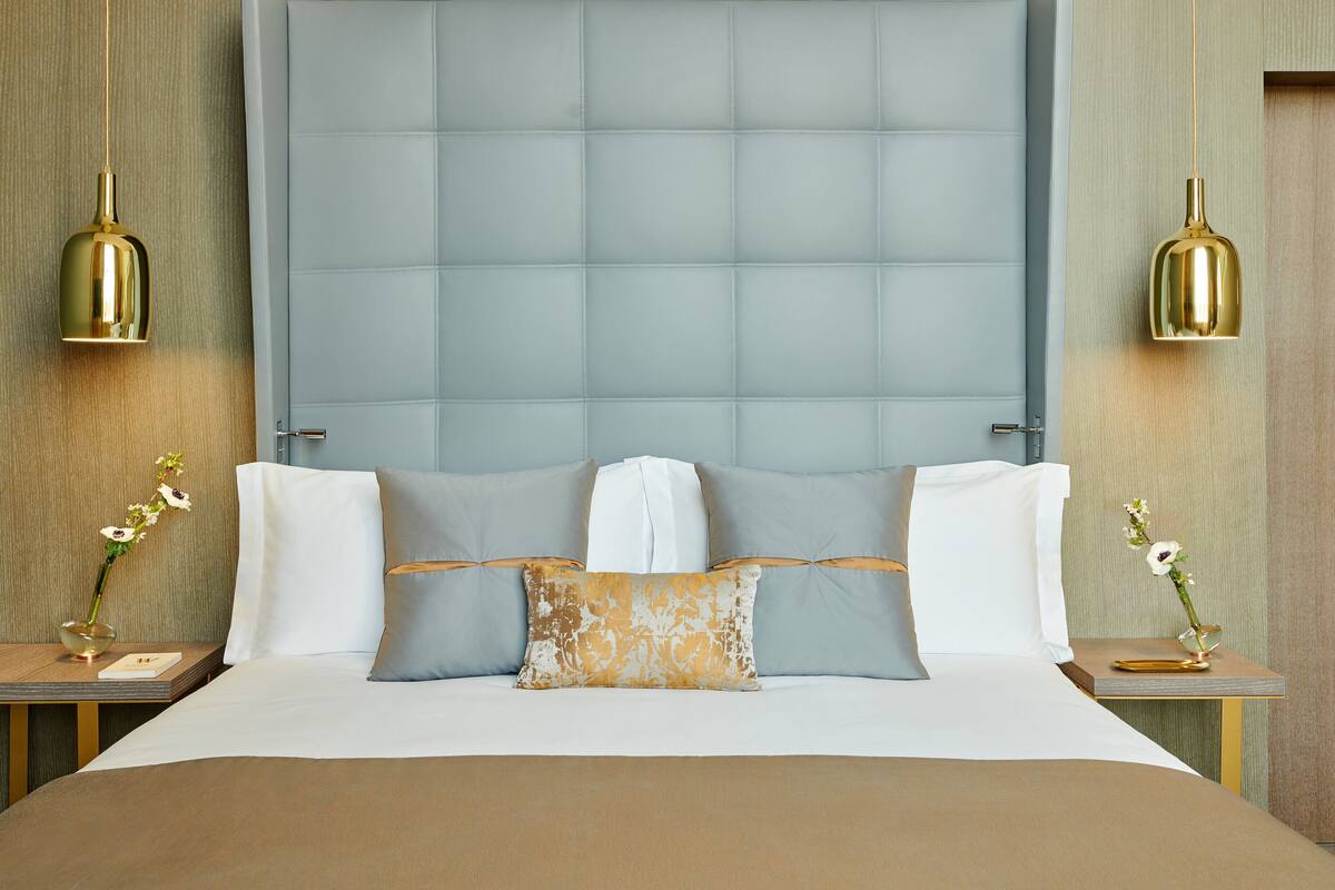 A neatly made bed with a large headboard, two bedside tables with lamps, and a vase with flowers on each side.