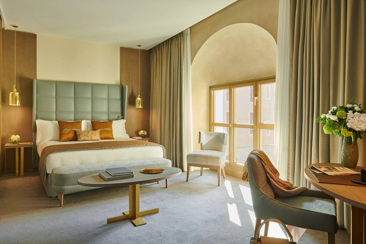 A modern hotel room with a large bed, a sitting area, and a desk.