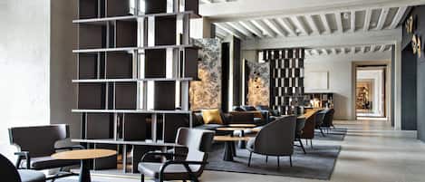 A modern interior with a central bookshelf, seating area, and a view into a dining space.