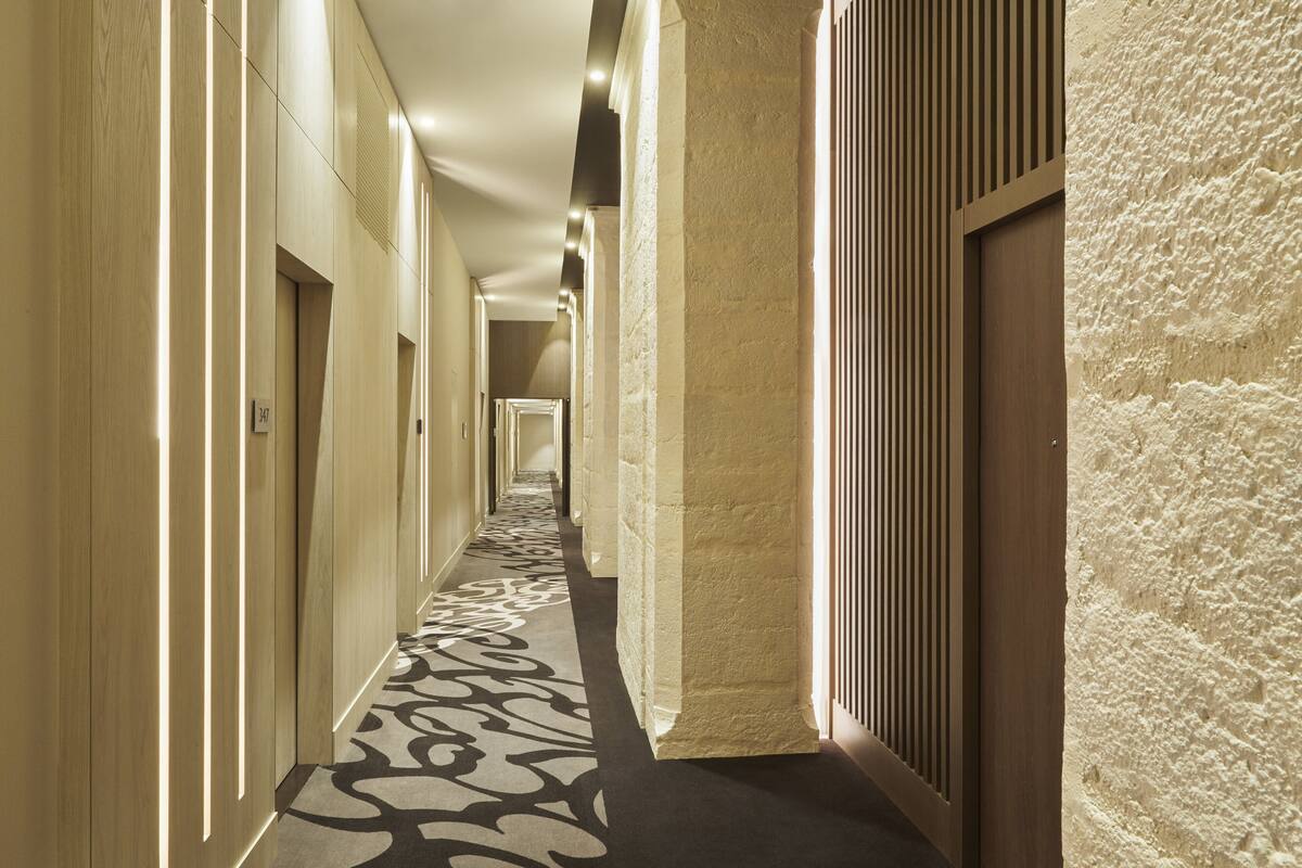 A long, narrow hallway with a patterned carpet, wooden walls, and a textured wall on one side.