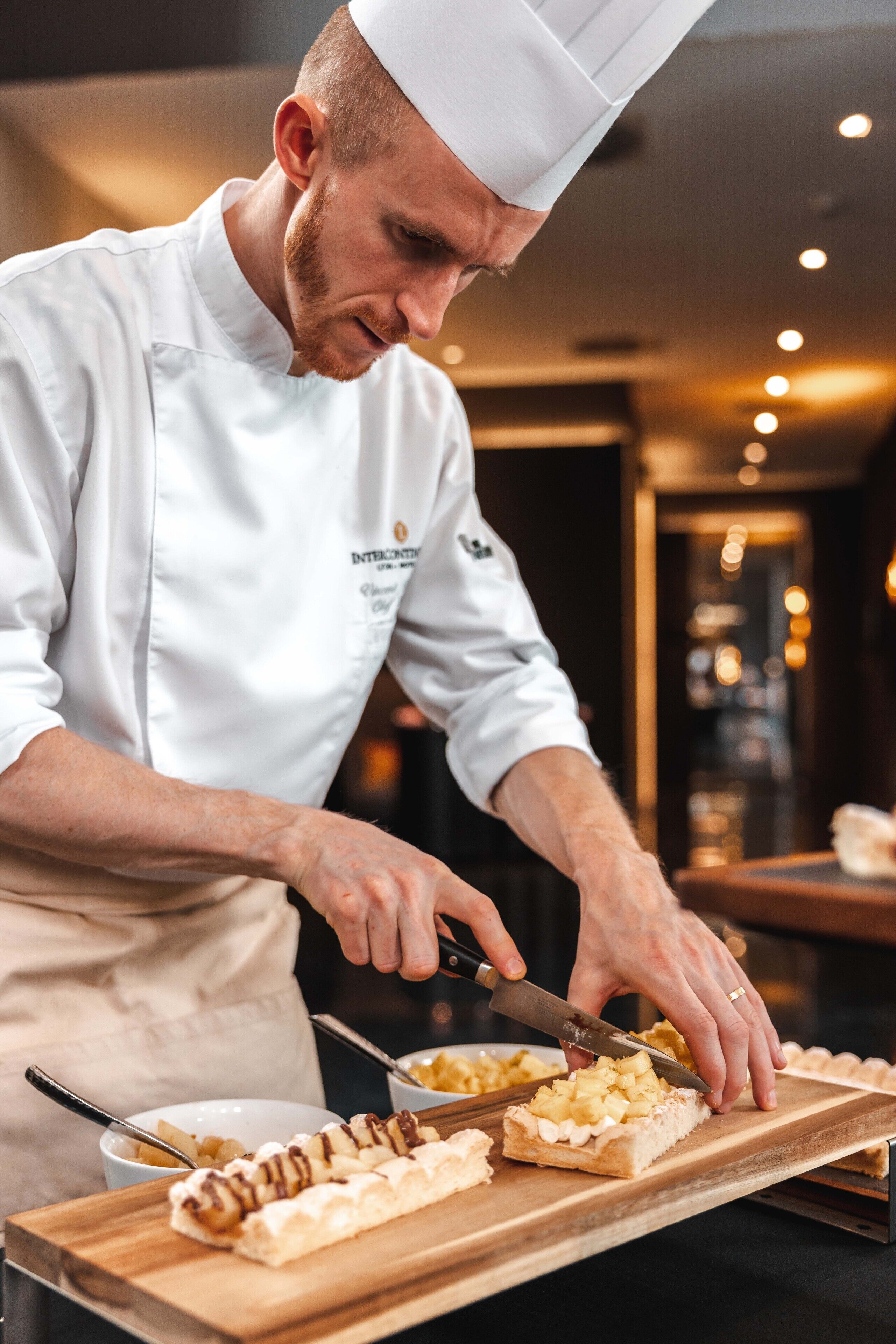 A chef in a white uniform preparing food on a wooden board.