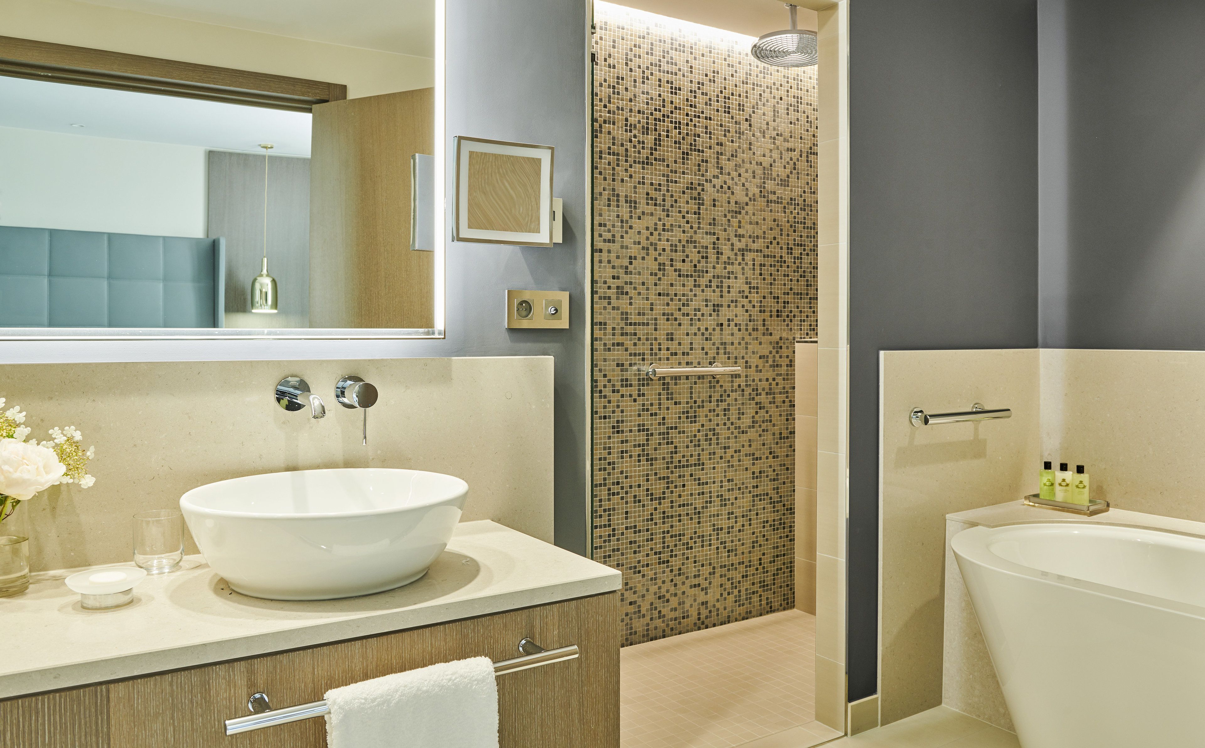 A modern bathroom with a large white sink, a bathtub, and a shower with mosaic tiles.