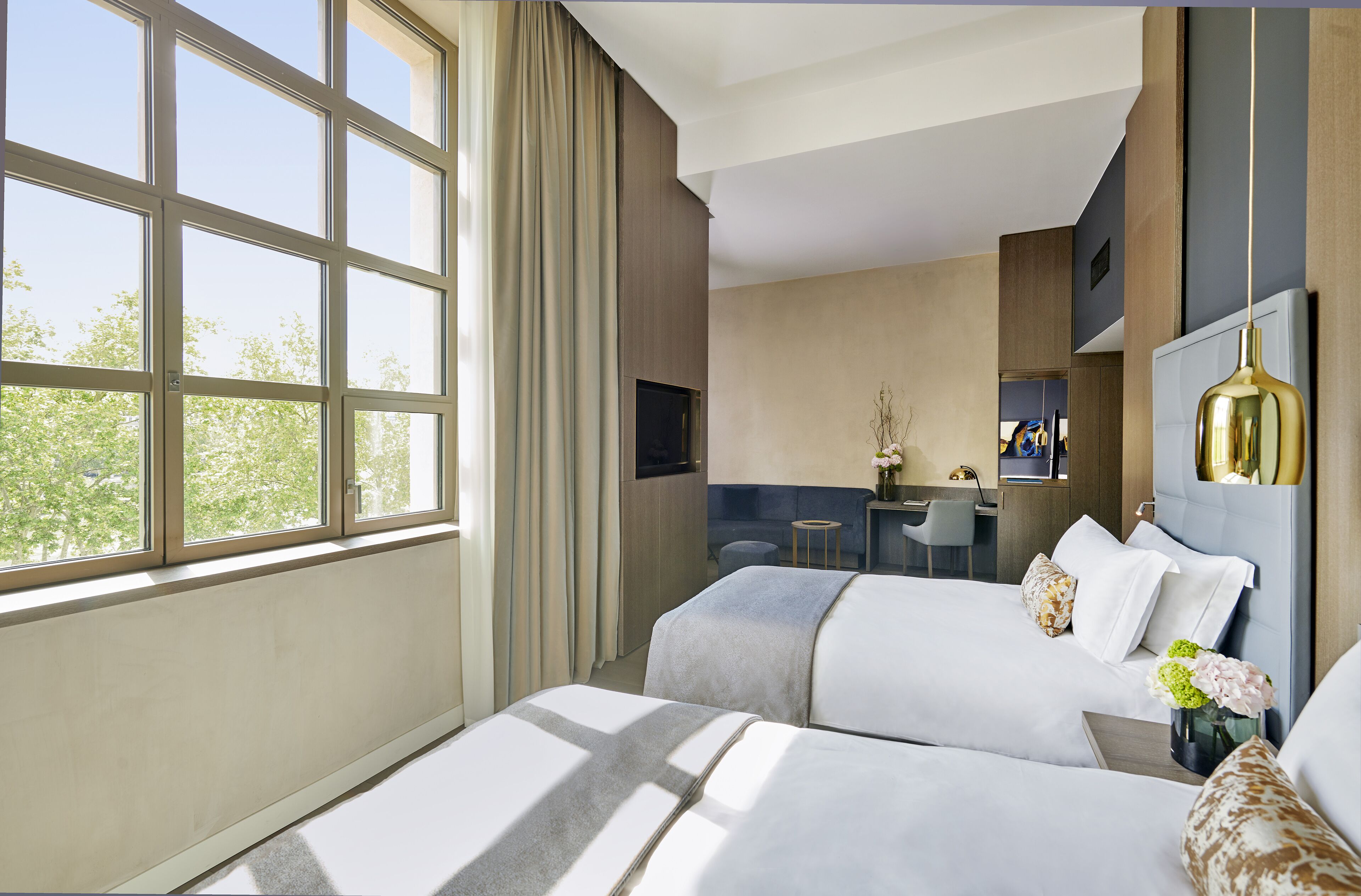 Habitación de hotel con dos camas, un escritorio, una silla y un ventanal con cortinas.