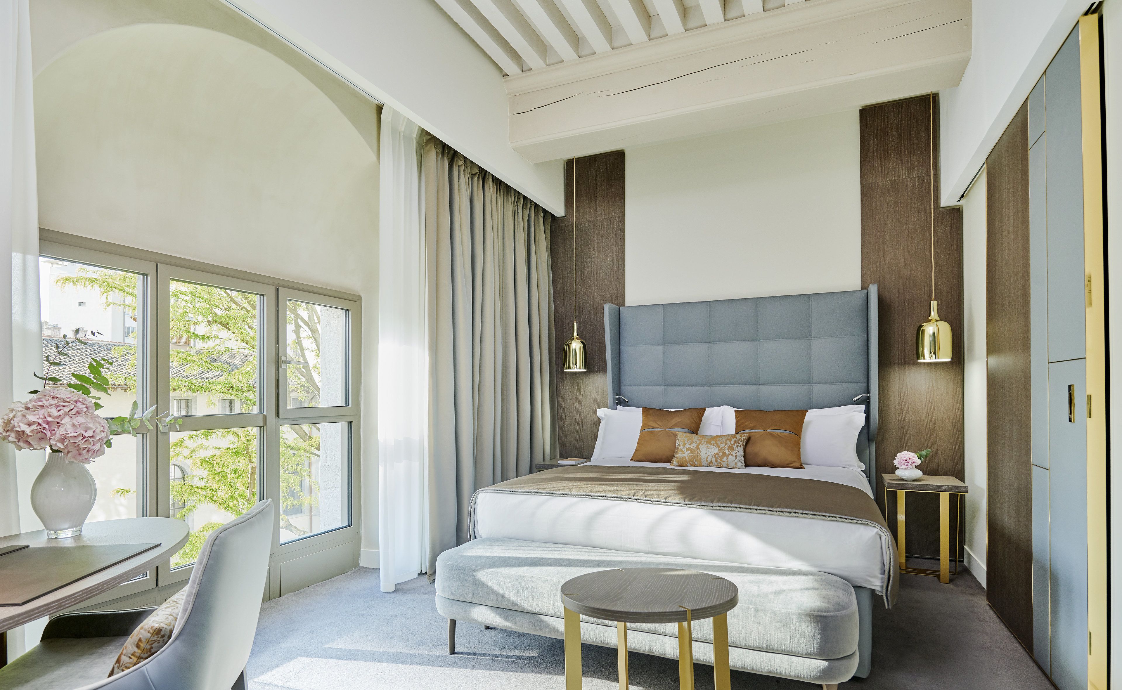 A modern bedroom with a large bed, bedside tables, a desk, and a chair.
