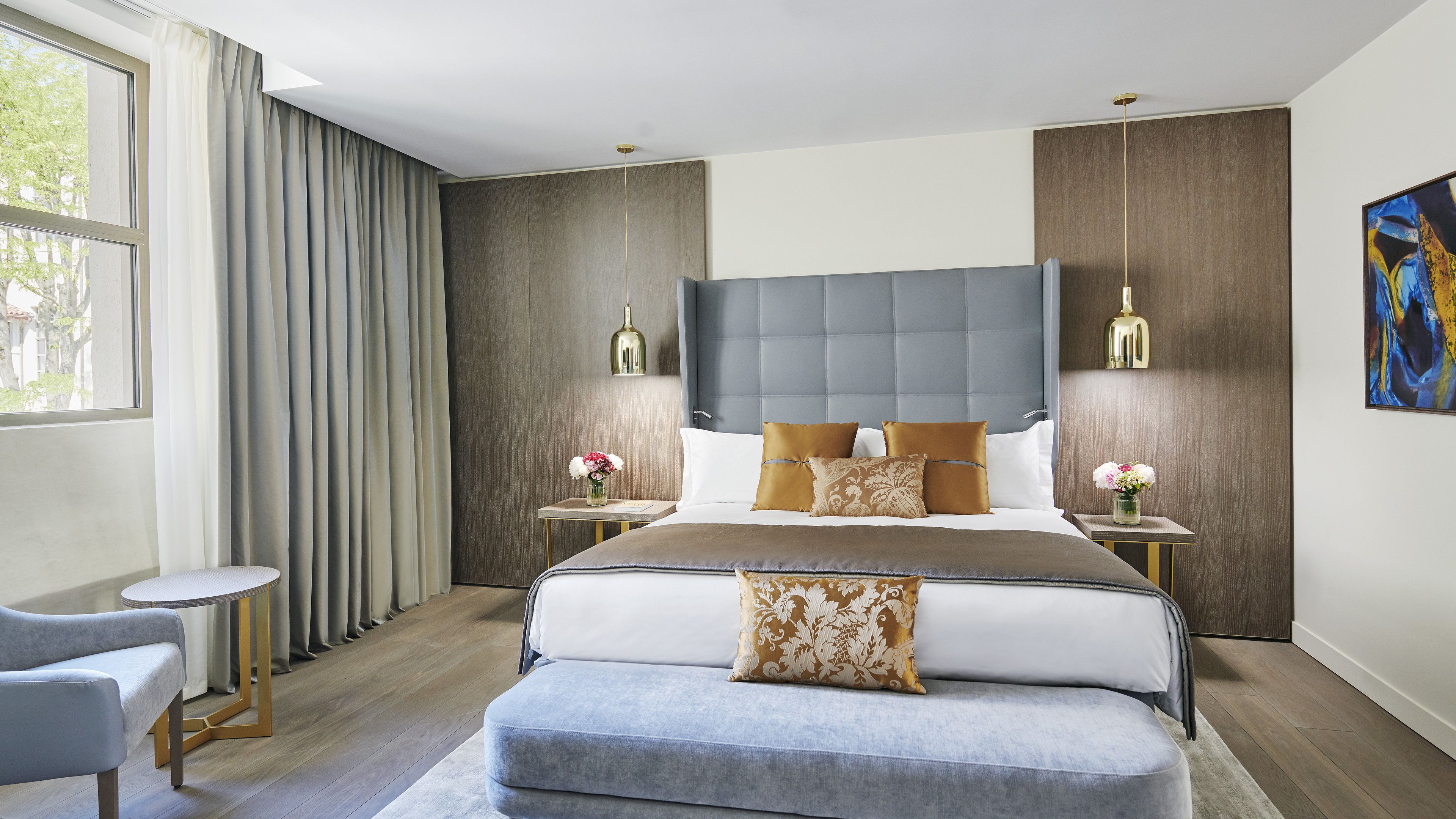 A modern bedroom with a large bed, two bedside tables, a small round table, and a bench.