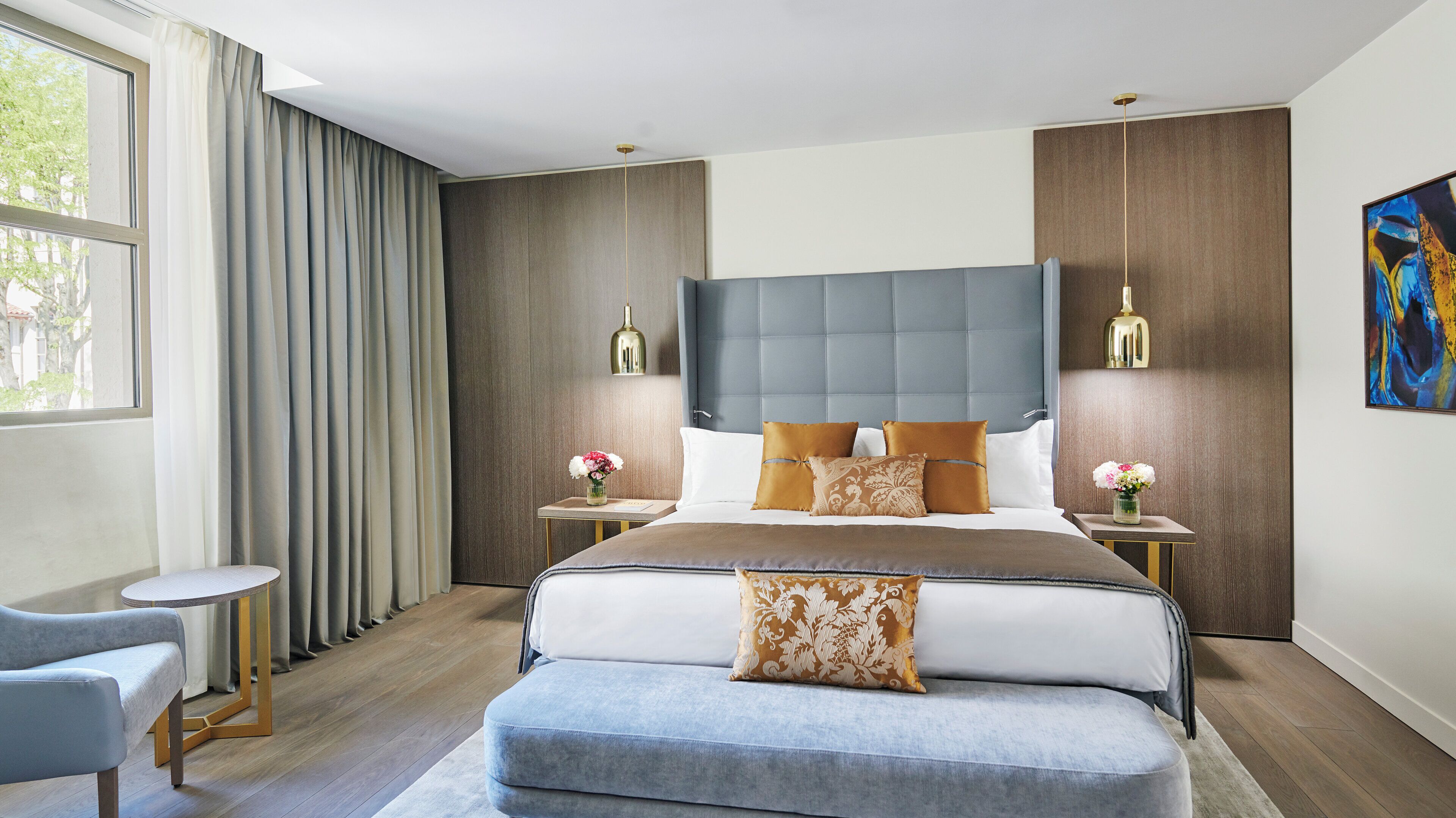 Une chambre à coucher moderne avec un grand lit, deux tables de chevet, une chaise et un tableau au mur.