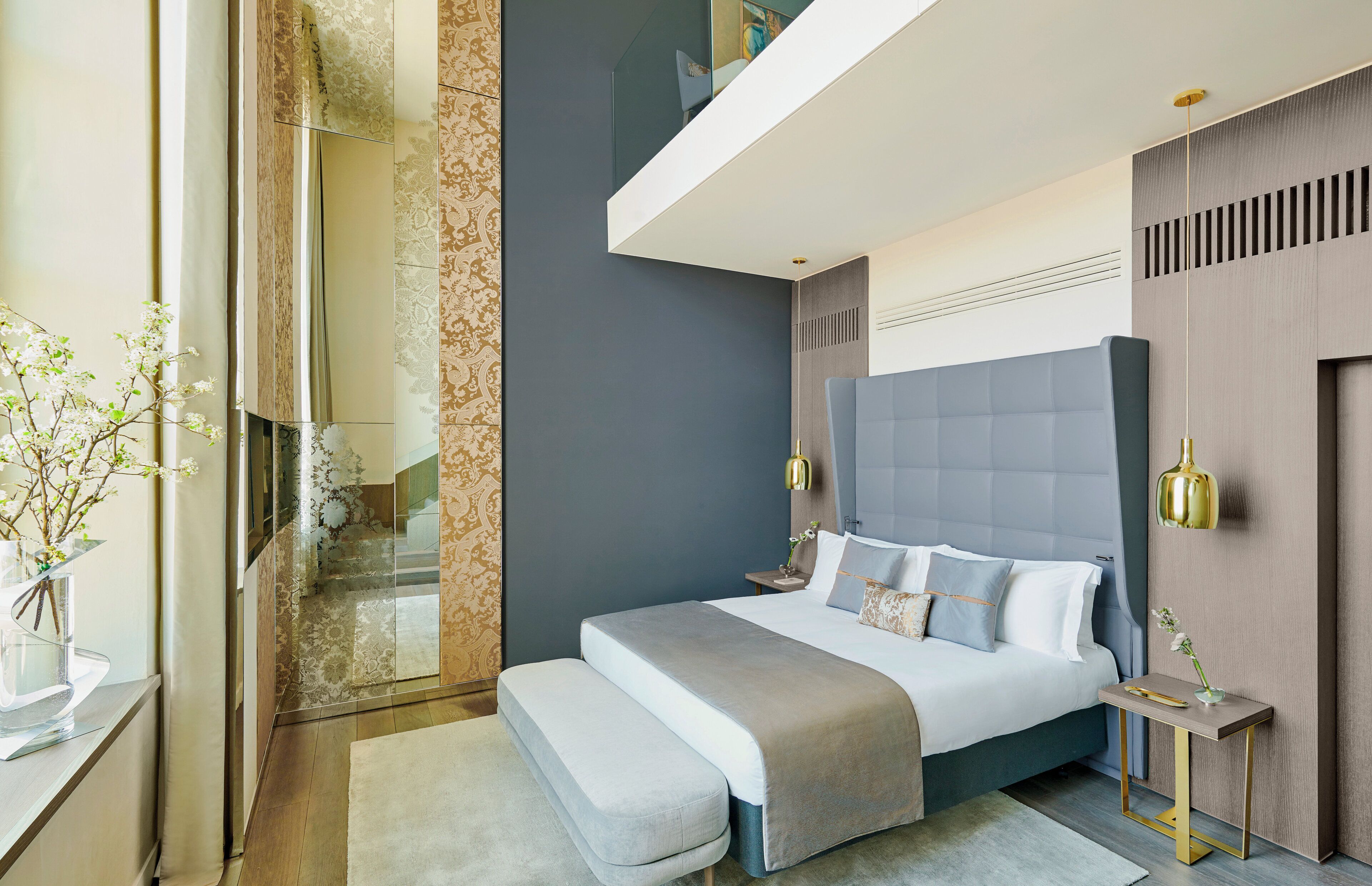 A modern bedroom with a large bed, bedside tables, a bench, and a glass shower enclosure.