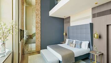A modern bedroom with a large bed, bedside tables, a bench, and a glass shower enclosure.