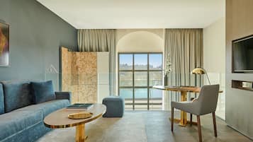 Una sala de estar moderna con un sofá, una mesa redonda de centro, una mesita auxiliar, una silla, un televisor y un ventanal con vistas.