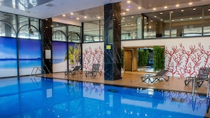 An indoor swimming pool with clear blue water, surrounded by glass walls and a modern design. - Ramada by Wyndham Tire (Tire)