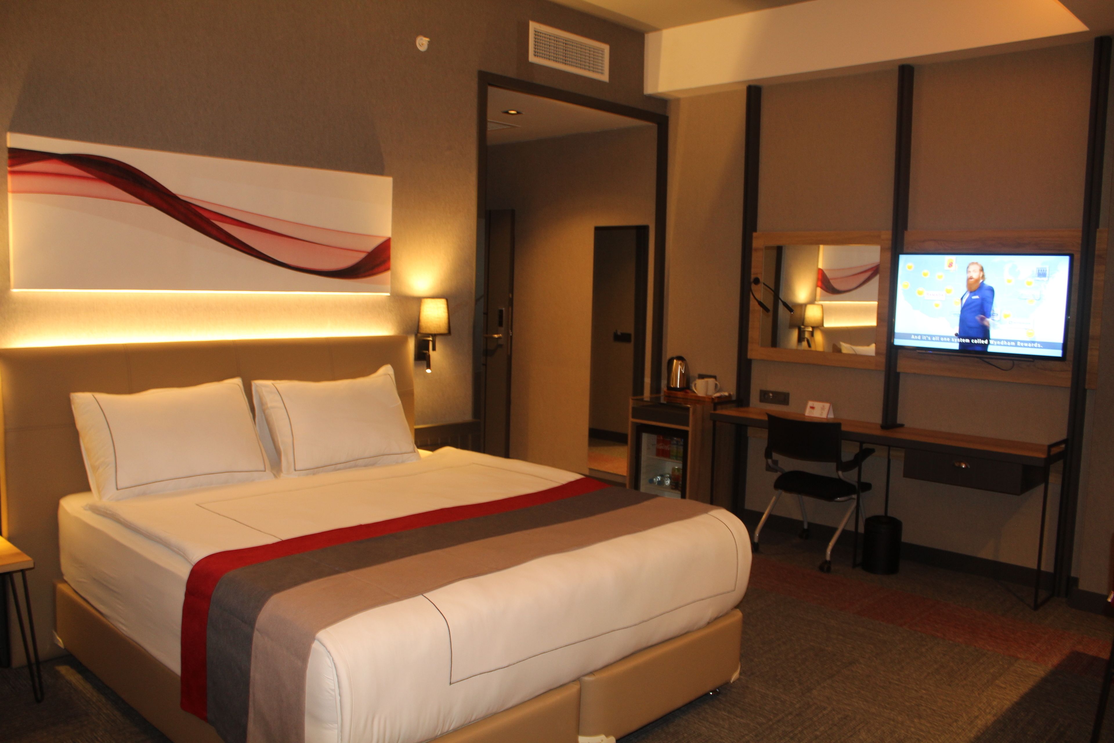 Habitación de hotel con una cama grande, un escritorio con computadora, televisor y una obra de arte colgada en la pared.