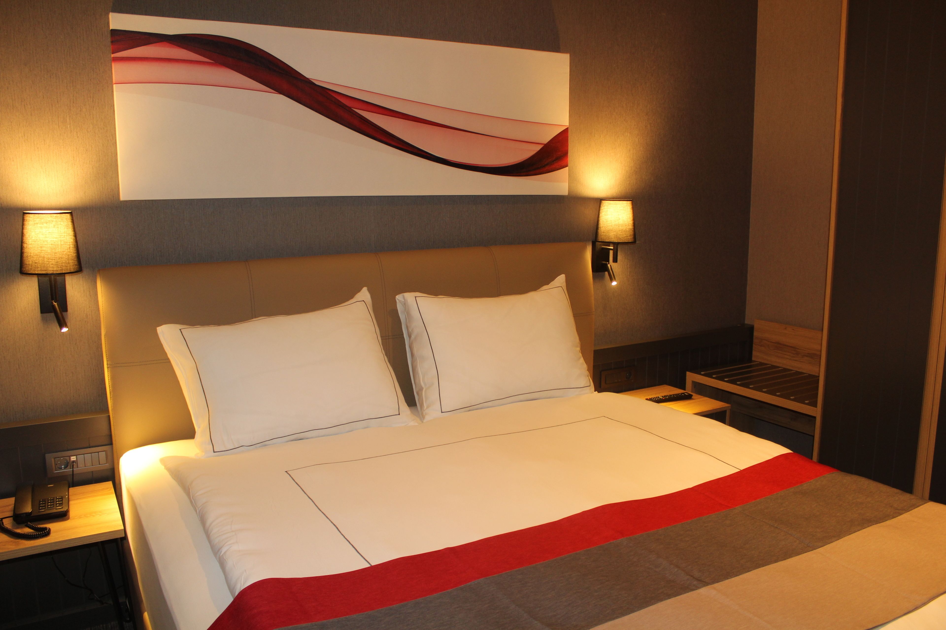 A hotel room with a large bed, two bedside lamps, a phone on the nightstand, and a wall-mounted artwork.