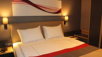 A hotel room with a large bed, two bedside lamps, a phone on the nightstand, and a wall-mounted artwork.